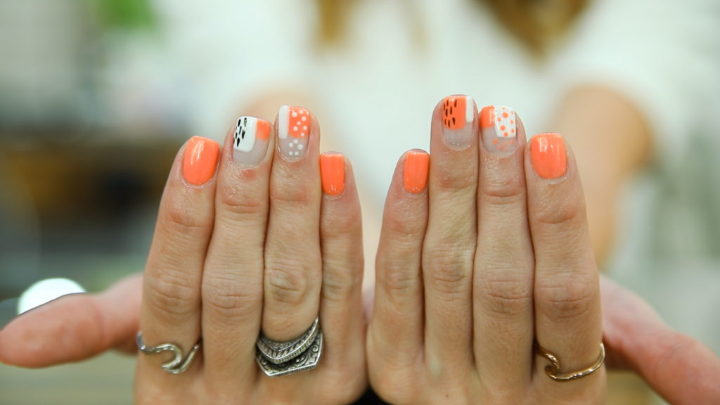 Woman's hands displaying orange and white nail art