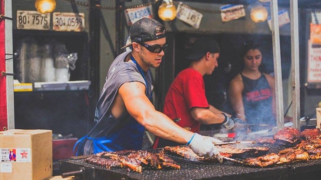 Man grilling ribs outside at a festival