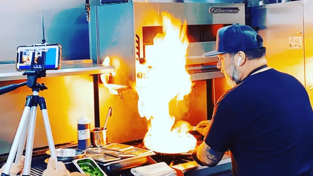 Photo of a chef working in a kitchen with a flame rising from a pan