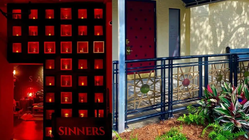 Interior and exterior of a new speakeasy with red lighting, a wall of candles and exterior green landscaping