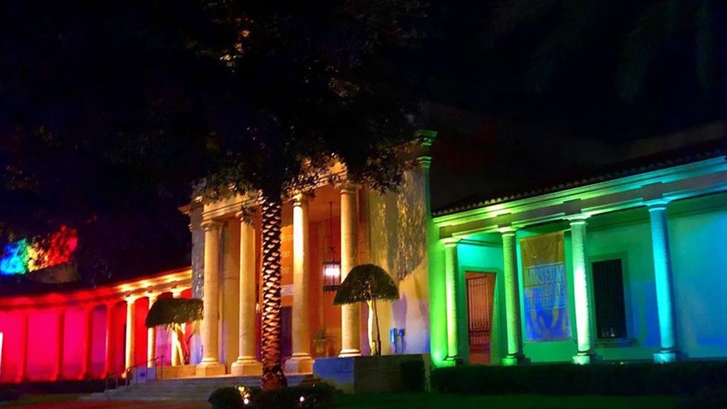 Rainbow lights projected on the exterior of a waterfront museum at night