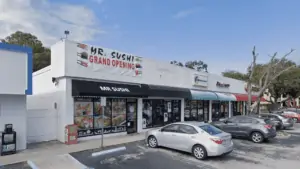 Exterior of a Strip Mall with a Sushi Banner, and several cars parked out front