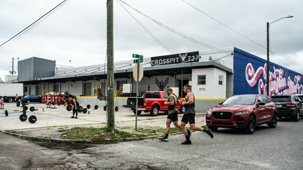 Two CrossFit members running outside next to a blue and pink mural