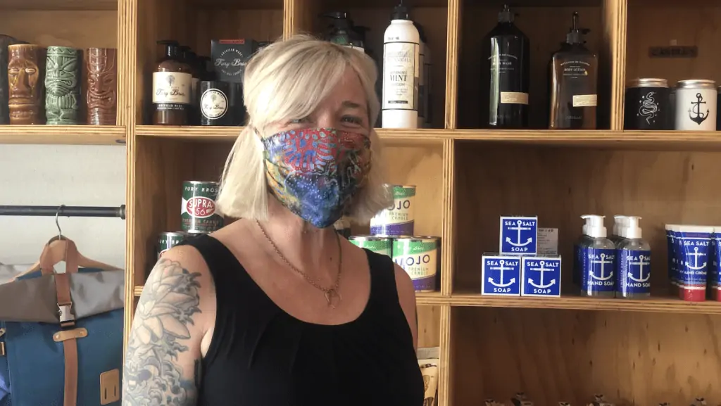 Photo of a business owner with tattoos on her left arm standing in front of shelves filled with candles