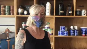 Photo of a business owner with tattoos on her left arm standing in front of shelves filled with candles