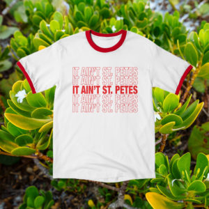 it ain't st. pete's white t-shirt with red ringer collar and sleeves on a background of greenery