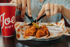 Someone cuts into a Joella's Hot Chicken lunch meal featuring large chicken tenders and green beans