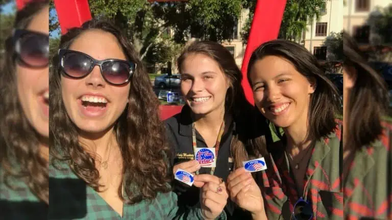 Three individuals holding I Voted stickers outside their polling place