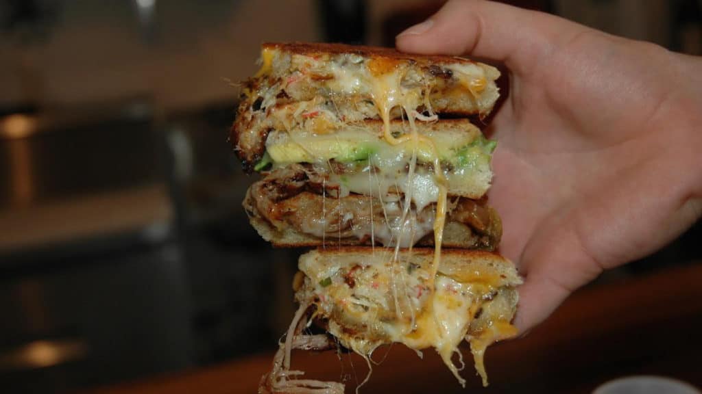 one hand holds melty gooey grilled cheese sandwiches stacked together