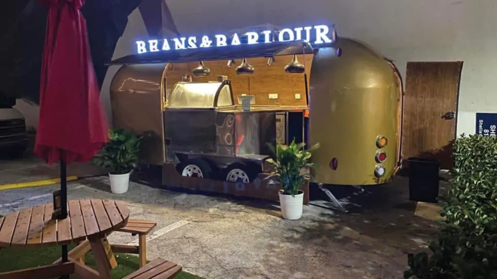 a golden airstream trailer with a "beans and barlour" sign on top and ice cream service inside