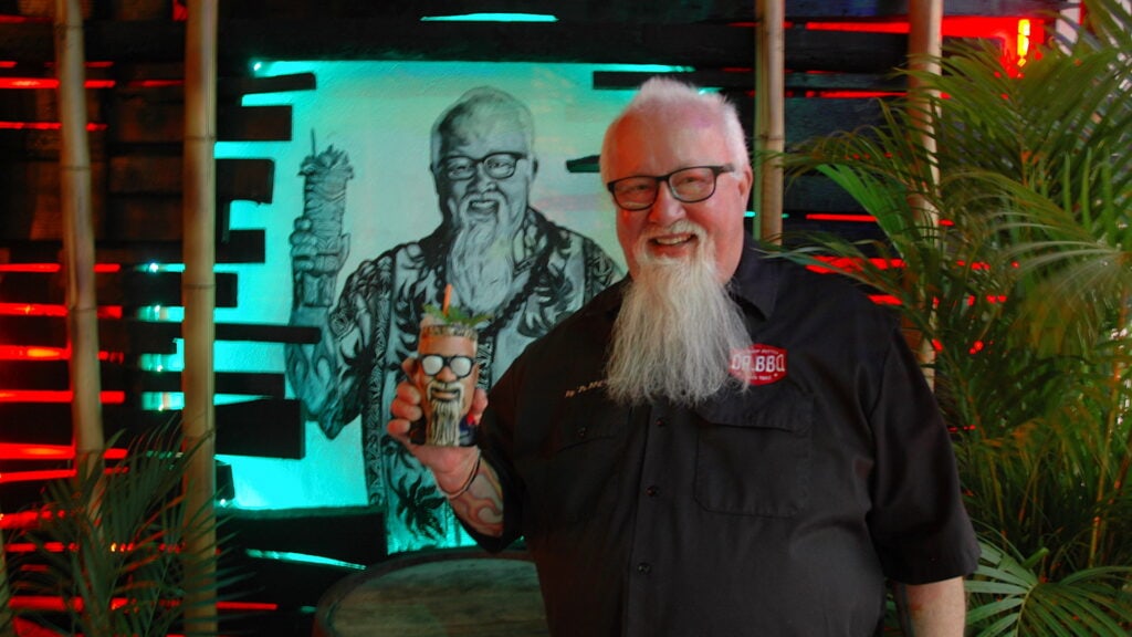 Man standing in front of a painting of himself holding a tiki cup