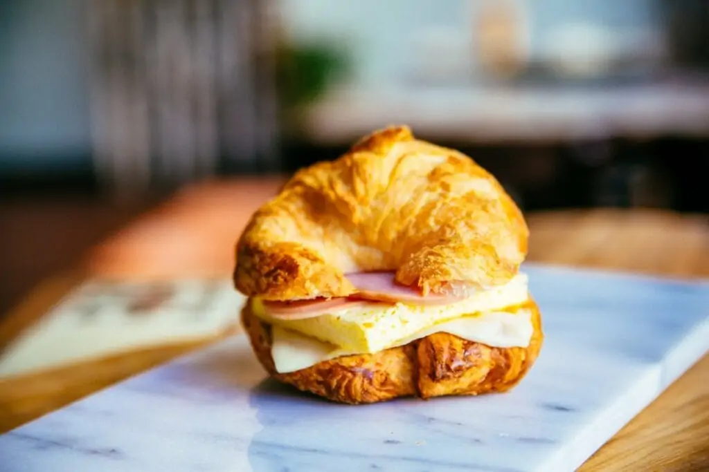a croissant sandwich with eggs and ham on a plate. 