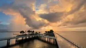 giant clouds at sunrise with a small pier in the distance