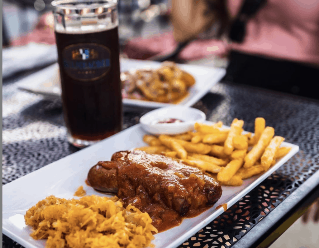 sausage and French fries on a plate in front of a tall beer glass.