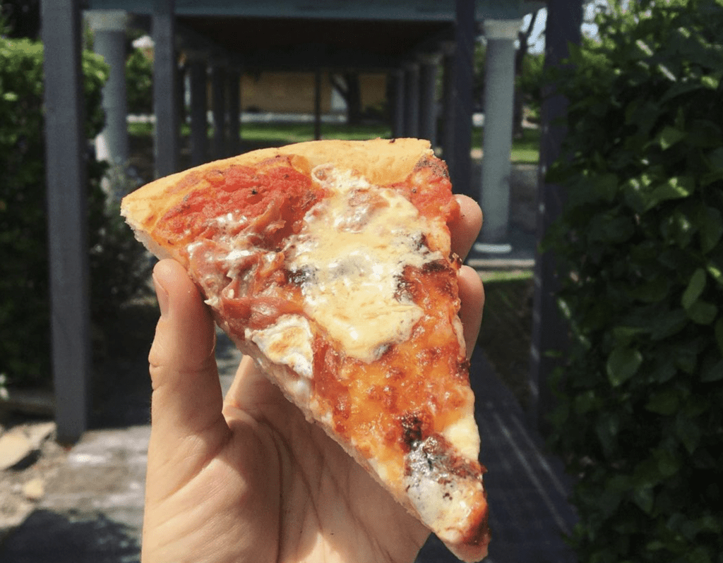 a large slice of pizza held in front of a restaurant door.