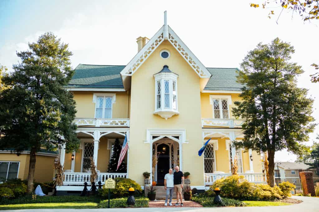Exterior of a gothic style home with yellow paint and a wrap around front porch. 