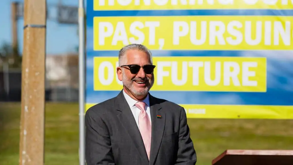 a man in sunglasses stand outside in front of a yellow and blue sign