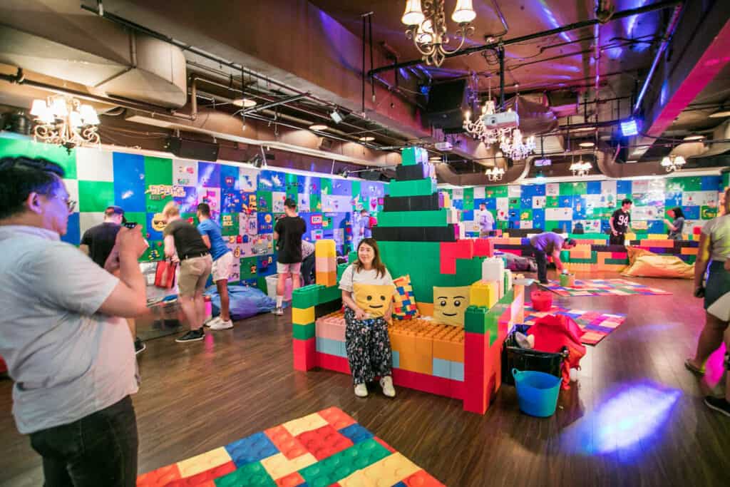 A large bar filled with colorful building blocks, with one person sitting on a couch made of bricks. 