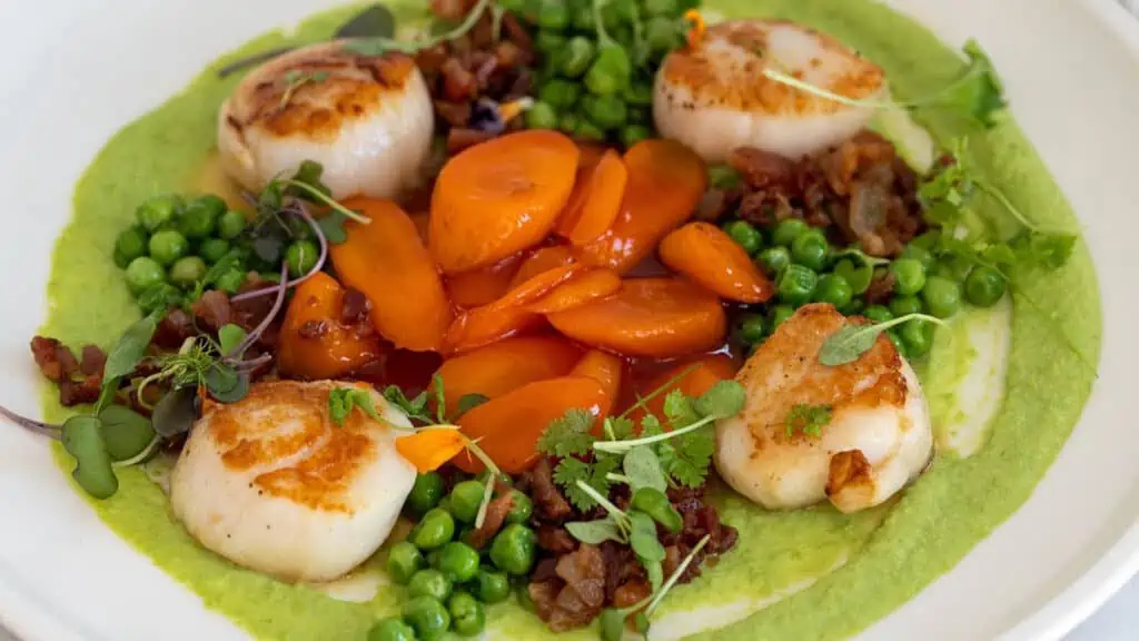 scallops, carrots, peas, and other veggies on a plate at cassis