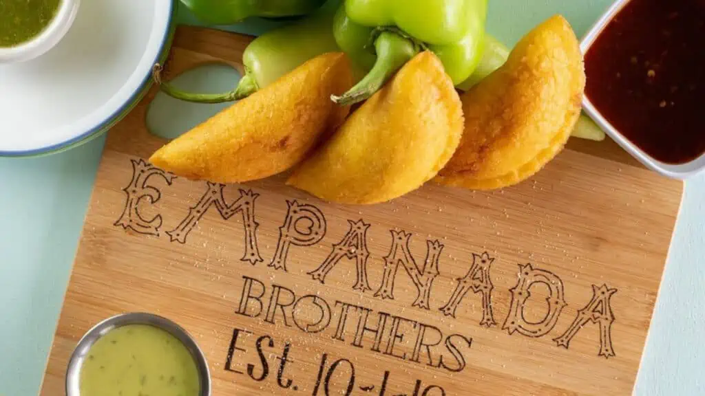 three empanadas and sauces on a cutting board that reads empanada brothers