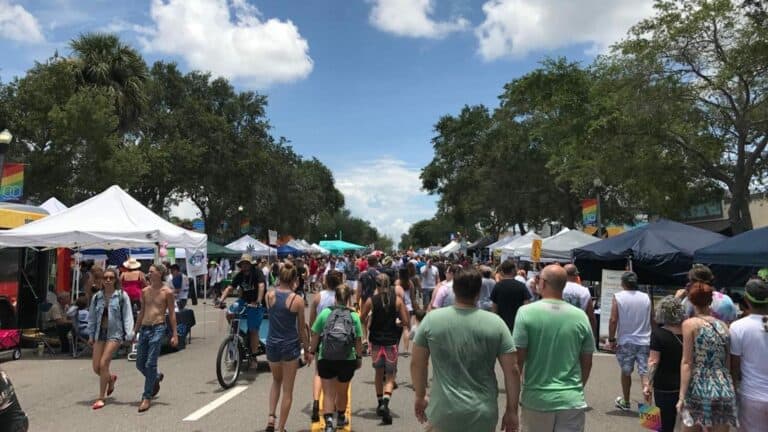 Image of St. Pete Pride parade on Central Avenue with tents and crowds of people walking
