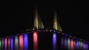 tall pride with rainbow lights underneath the bridge. Tall yellow poles protrude from the bridge.