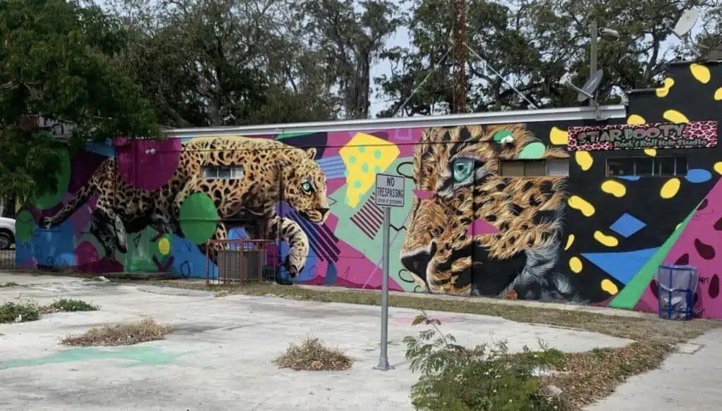 A mural with two cheetahs painted on the side. Purple, teal, black and yellow all mix in the background to form a geometric canvas. 