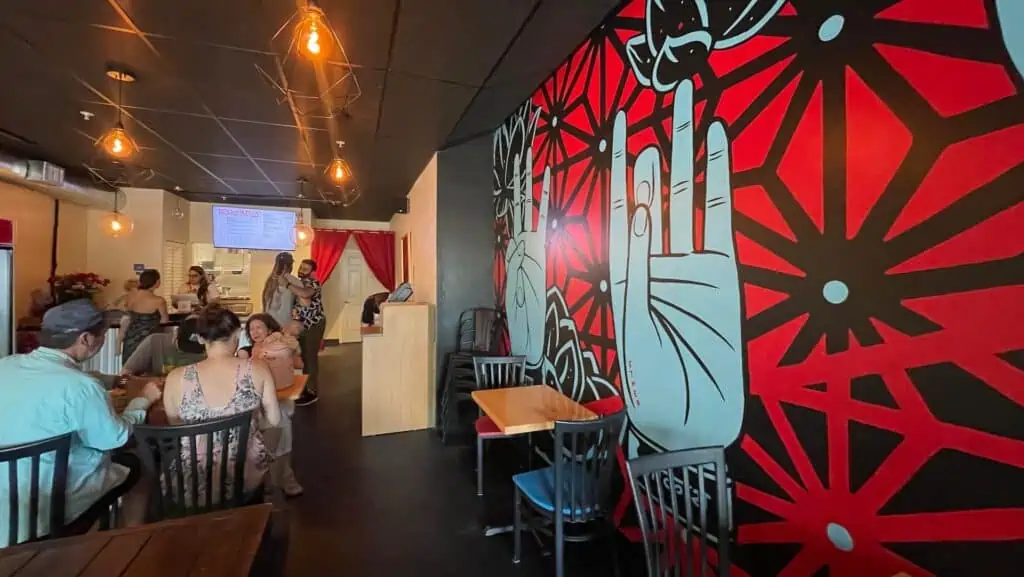 inside a small restaurant with a mural featuring blue hands and red flowers on the wall