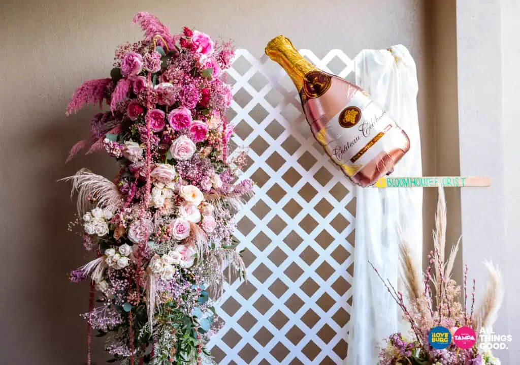 a cascading bunch of pink flowers and a champagne balloon on a flower wall