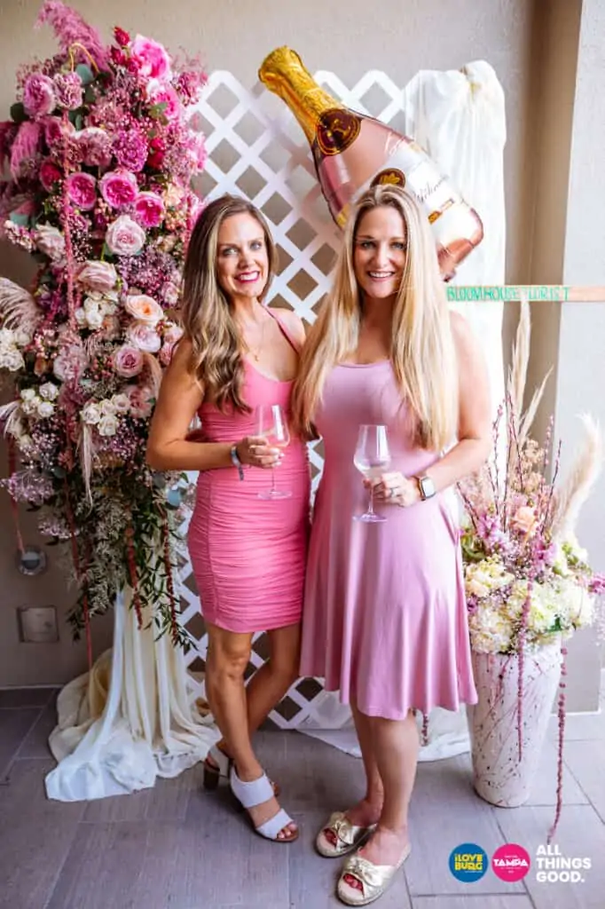 two friends pose in front of the flower wall at rose by the bay