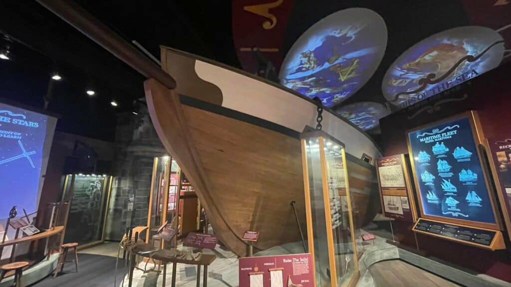 A large sail boat set inside a museum exhibit space with a night sky projected on the ceiling