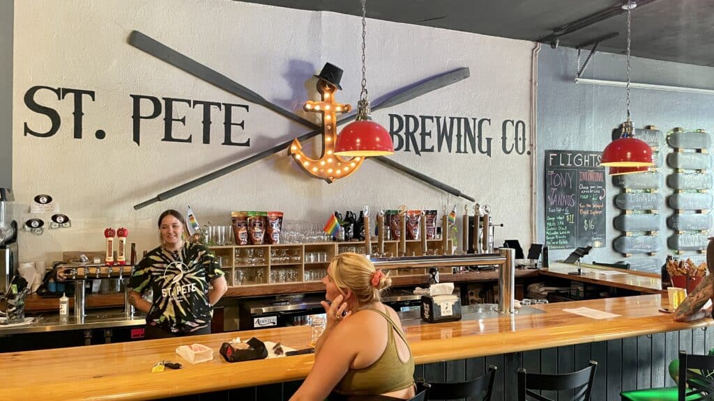 A bartender and a guest sitting inside St. Pete Brewing Company
