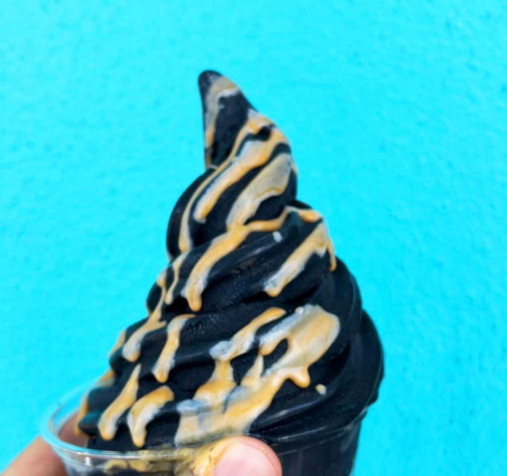 a cup of dark ice cream covered in peanutbutter set in front of a blue wall