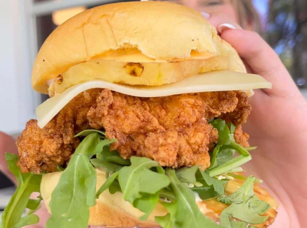 large fried chicken sandwich with lettuce on the bottom and cheese and pineapple on the top. 