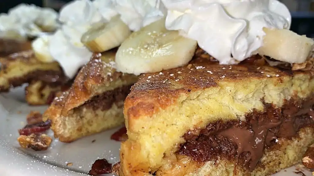 Three thick pieces of French toast stuffed with Nutella and banana and topped with whipped cream.