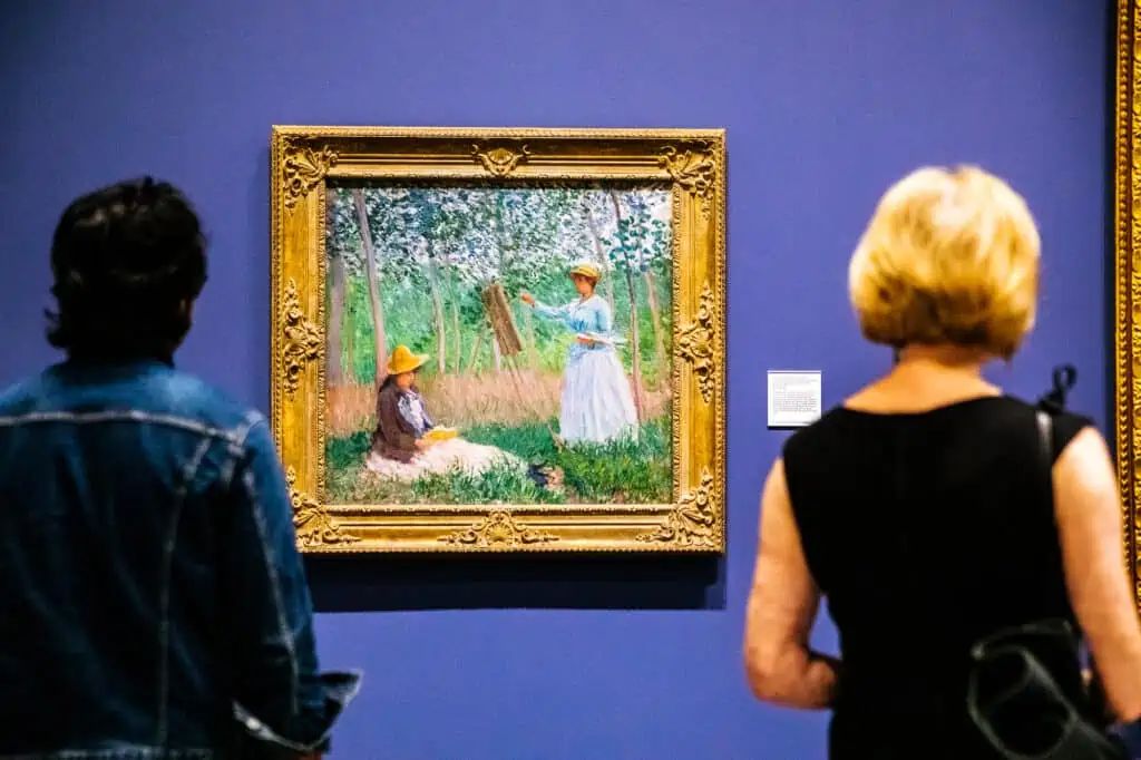 two people look at an impressionist paintings of two girls in a field painting.