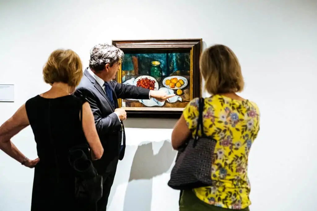 A group of people look at a painting of fruit by Cezanne