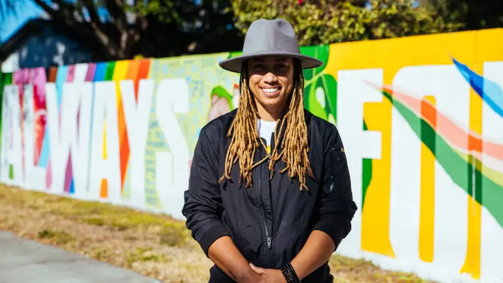 Artist Jones smiles while standing in front of their first mural in tampa bay