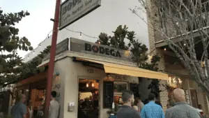 Exterior of a walk up restaurant with a yellow awning. People lineup at the order window.