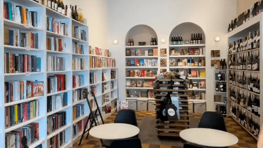 inside a book shop and wine shop. Rows of books are on the left side, bottles of wine on the right side.