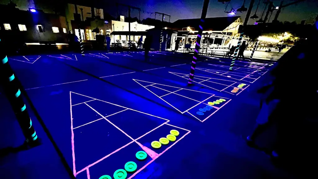 Glow paint on a shuffleboard court at night. The discs are also covered in glow paint. 4 courts are in view.