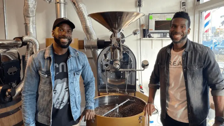 two men stand in front of a coffee roaster