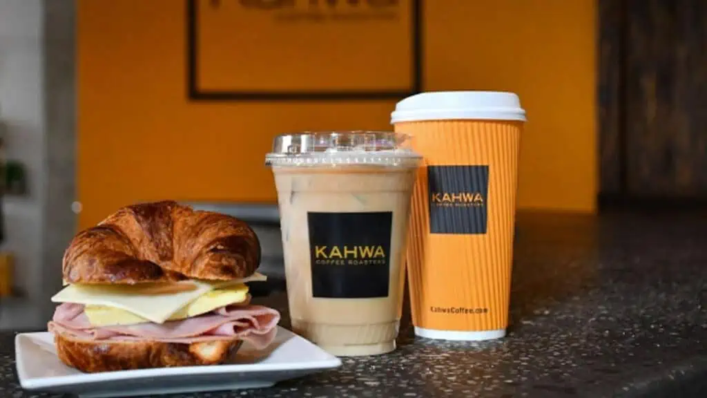 Ham, egg and cheese croissant next to an iced and hot coffee from Kahwa