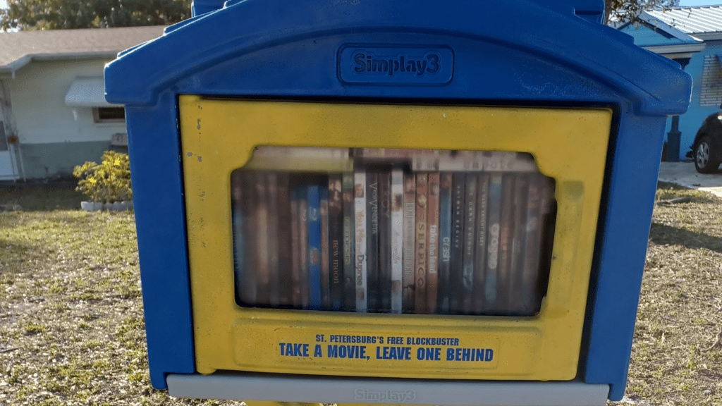 collection of DVDs inside a blue and yellow box on the front of a lawn.
