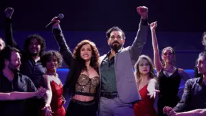 Two people raiser their hands at the center of a lit broadway stage