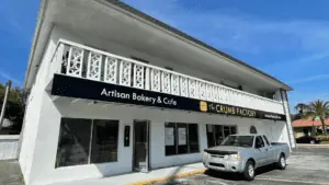 Exterior of a restaurant with a white paint job and a black and yellow awning. A truck is parked out front.