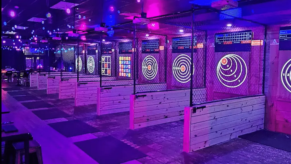 inside a glowing axe throwing venue. Games are projected on the