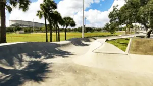 skatepark with a long bro bowl structure. A baseball stadium is visible in the background.