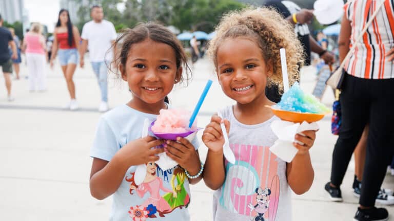 Two young children smiling while holding snow cones outdoor