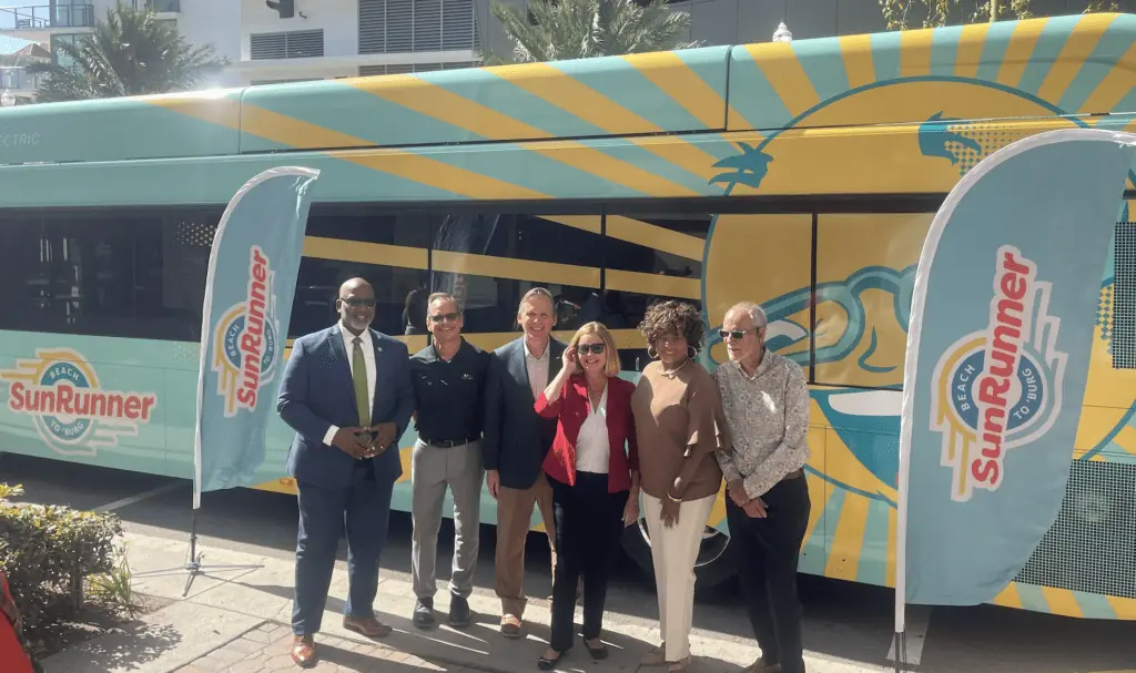 A GROUP OF PEOPLE STAND IN FRONT OF A BLUE BUS WITH A YELLOW SUN PAINTED ON THE SIDE